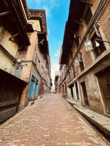 A narrow, cobblestone street flanked by traditional buildings with wooden balconies and windows.
