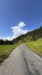A winding asphalt road leads into a lush green landscape with hills on either side.