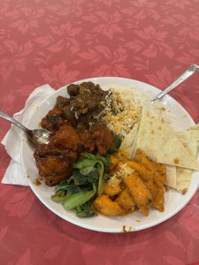 A plate with grilled chicken in sauce, meat with gravy, rice, and sautéed greens.