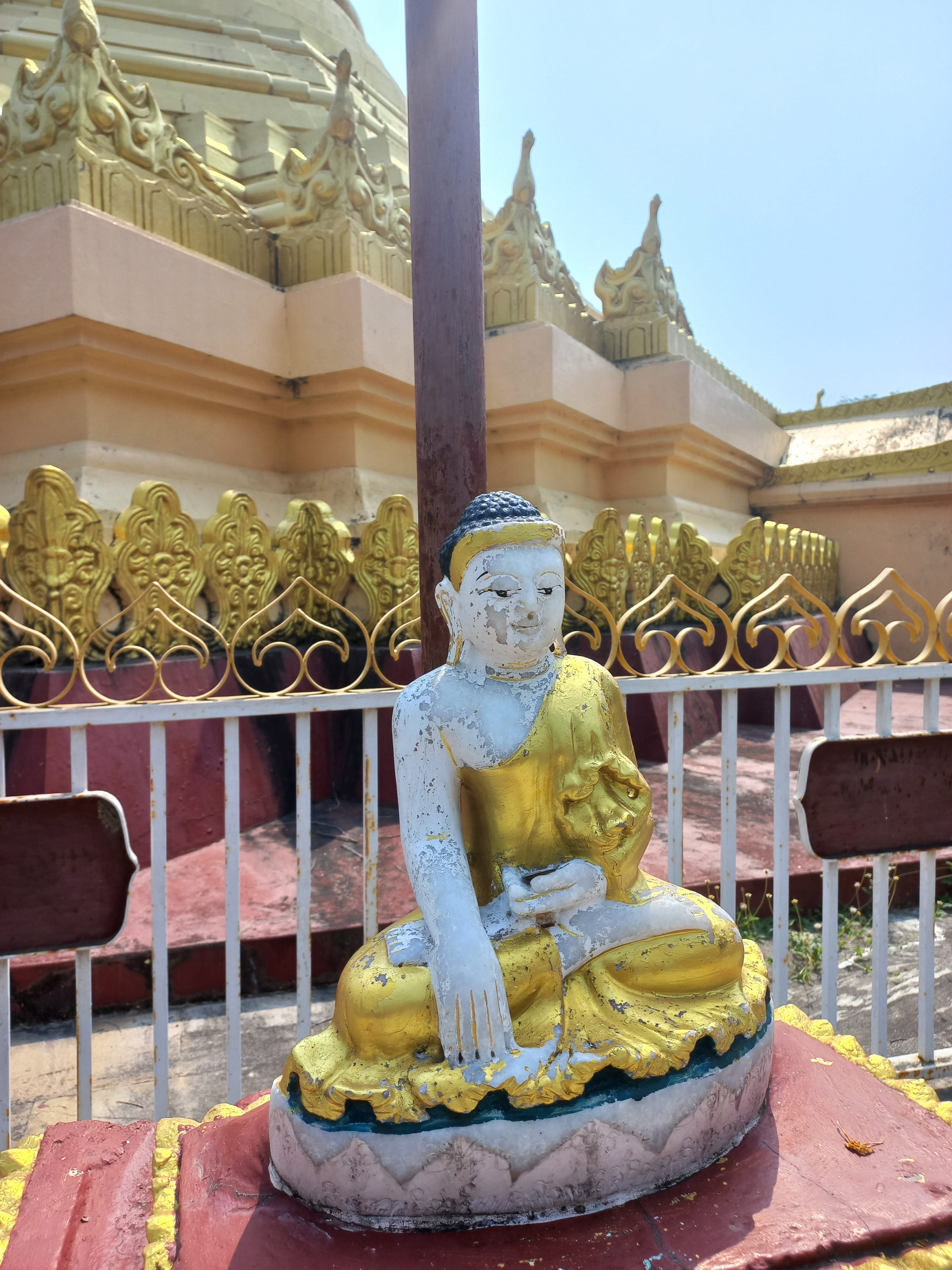 A weathered seated Buddha statue, partially gilded in gold, with a serene expression.