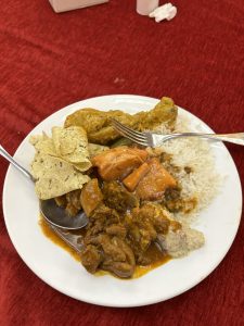 A white plate filled with a variety of foods, including pieces of yellow marinated mutton, rice, and a mix of curries