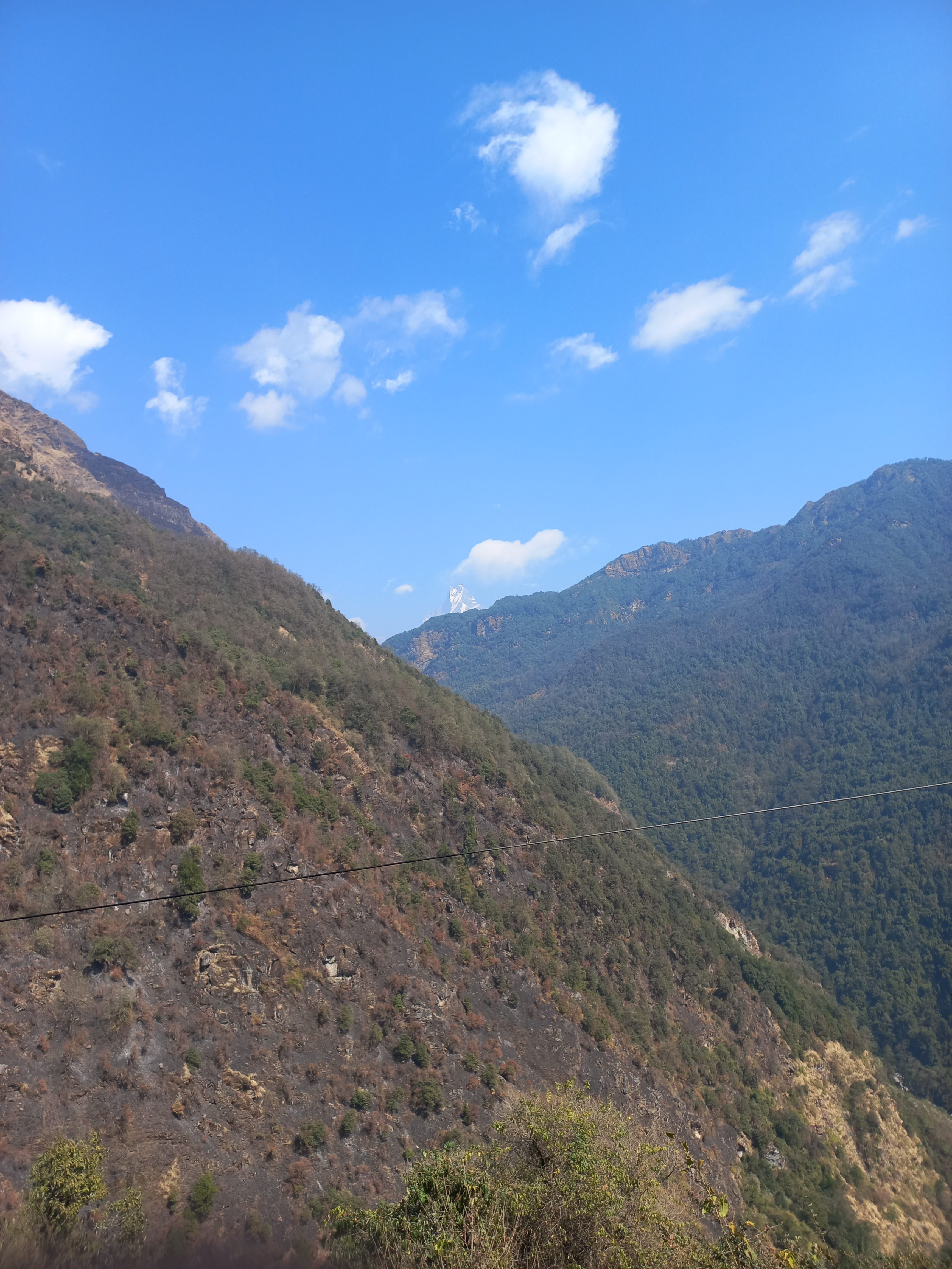 A panoramic view of mountainous terrain under a clear blue sky scattered with clouds.