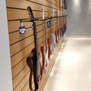 A variety of guitars hanging on a wooden wall display in a music store.
