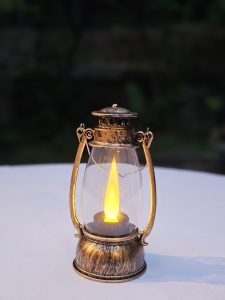 Antique-style lantern with a glowing flame-like LED light on a white tablecloth. Evening shot from Washington Park, Portland. 