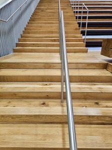 A staircase made of smooth wood with a central metal handrail inside Portland International Airport. The clean and modern steps lead up to the seating area, showcasing the terminal's wooden interior elements. 