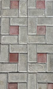 A close-up view of a decorative concrete pavement featuring a pattern of gray and red rectangular tiles.