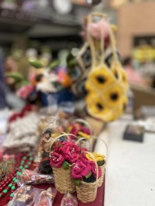 A market stall featuring small woven baskets filled with pink paper flowers and other handcrafted items.