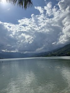 A serene fewa lake scene under a partly cloudy sky filled with dramatic, billowing clouds.