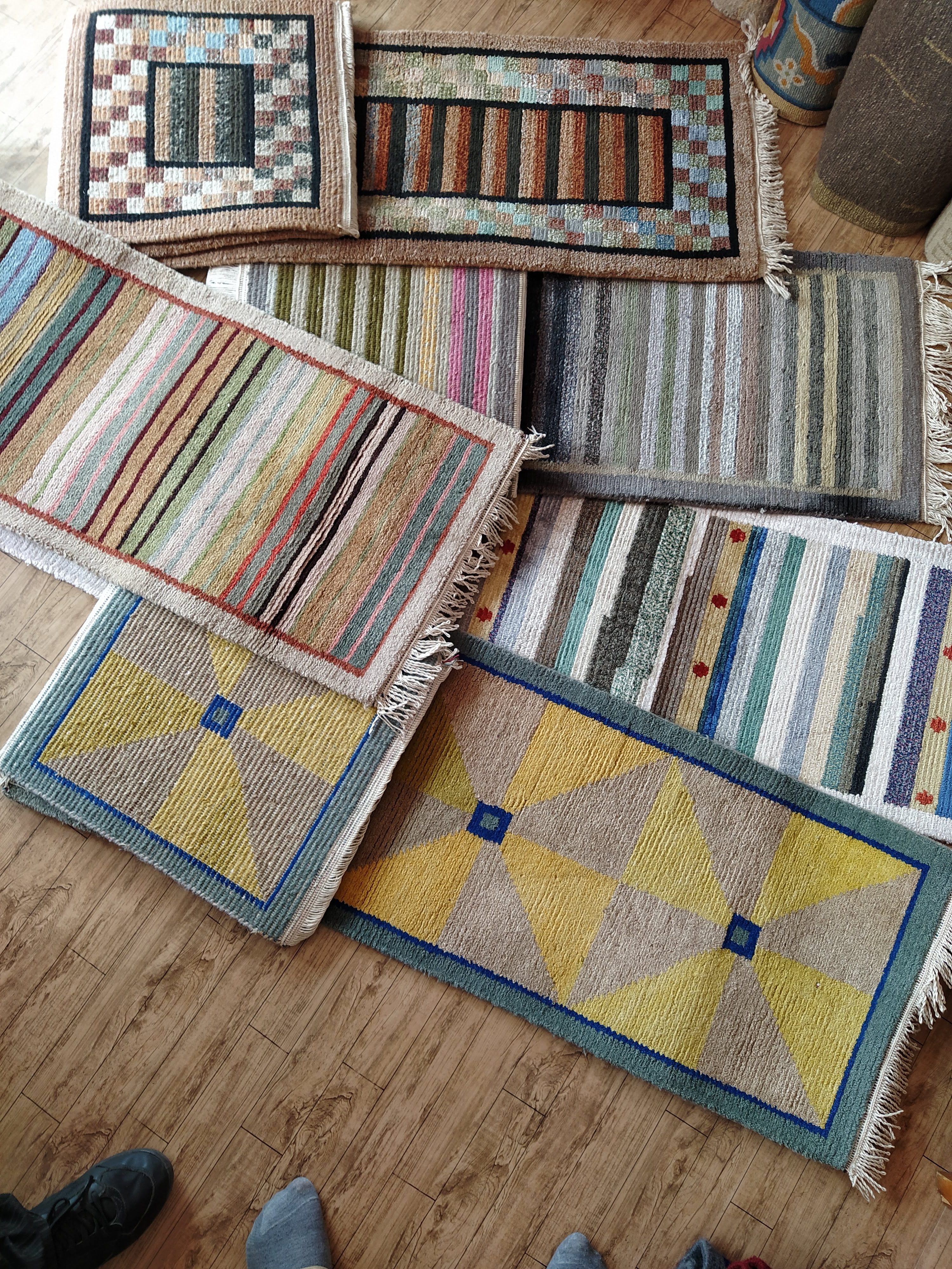 A collection of colorful, woven rugs laid out on a wooden floor, showcasing various geometric patterns and stripes.