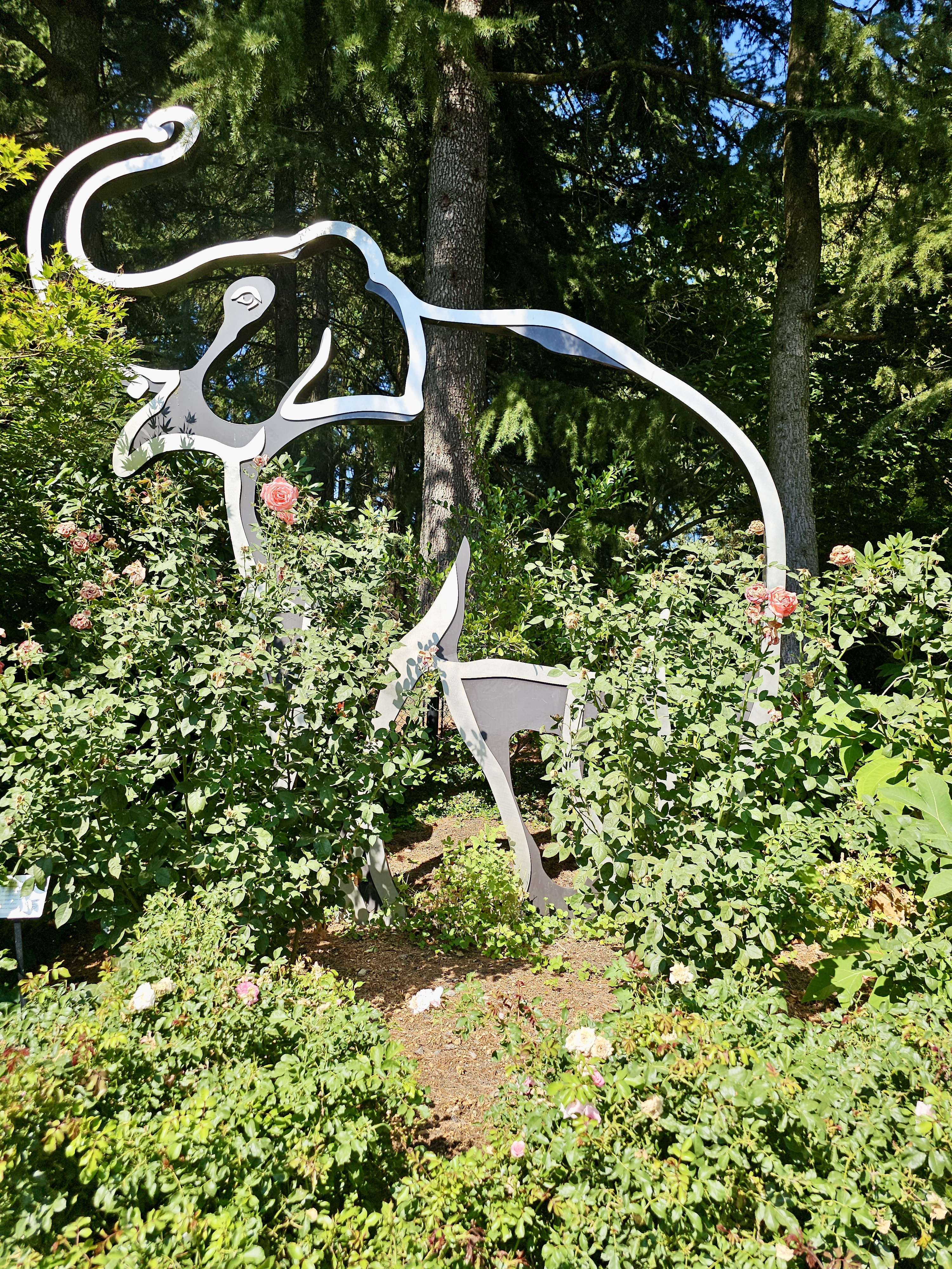 Close-up of elephant statue base, surrounded by ornamental grass, plants, and shaded by tall trees, captured from the Oregon Zoo, Portland. 