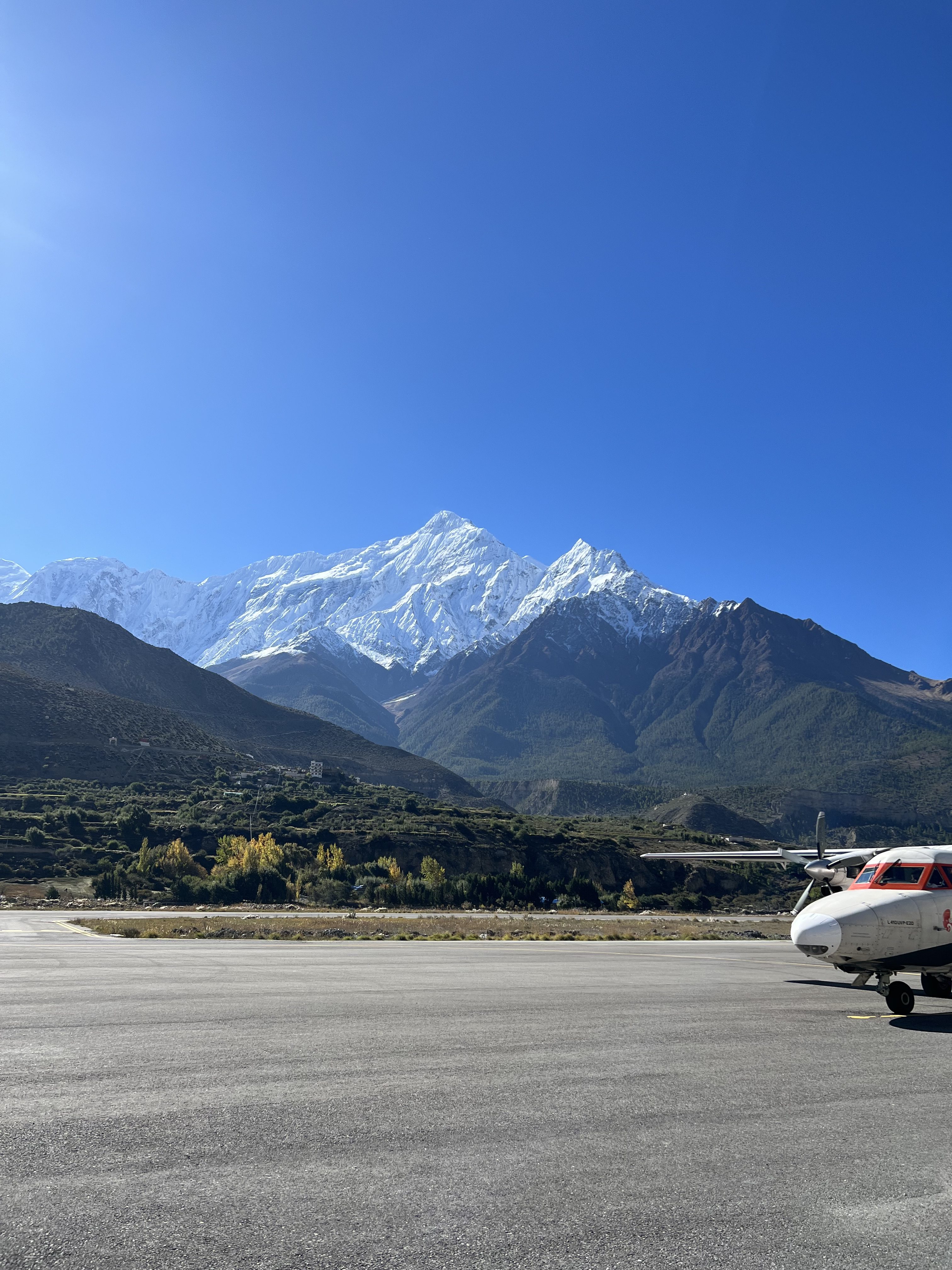 A ground-level shot of a small airplane parked on an airport tarmac with a large, snow-covered mountain range in the background.