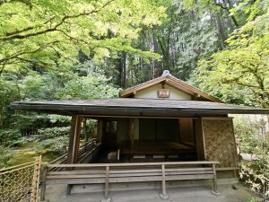 A peaceful Japanese tea house with an open wooden porch surrounded by tall green trees in Portland Japanese Garden.