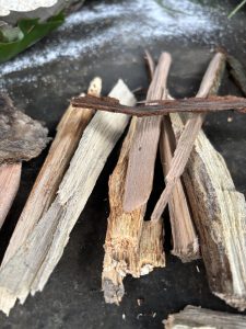 A collection of various pieces of wood, ranging from light beige to dark brown, is scattered across a dark, textured surface.