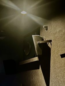 A spotlight illuminates a dark, textured wall with a security camera mounted near the ceiling.