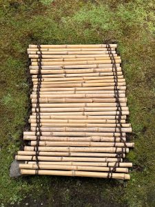 A handmade bamboo mat tied with rope, placed on mossy ground, photographed at the Portland Japanese Garden, Oregon. 