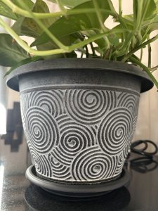 A decorative plant pot featuring a spiral pattern in black and white, with green plant leaves visible at the top.