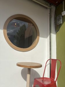 A round wooden-framed window is set into a white wall, providing a view of the outside