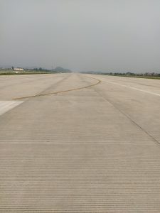 A wide view of an airport runway extending into the distance, with faint mountains visible in the background. 