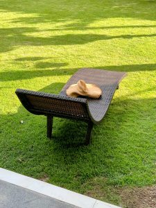 A straw sun hat rests on a curved black wicker lounge chair on a bright green lawn.
