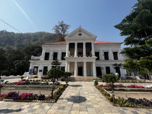 Rani Mahal, also called Ranighat Palace, is a significant historic palace from the Rana dynasty. It stands in the Palpa district of Nepal, beautifully situated right on the banks of the Kali Gandaki River. The image also includes green hills on its background,floor with stones and a beautiful garden.