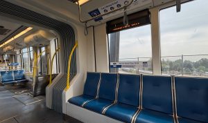 The inside of a metro train. On the right are some blue seats with a handle bar overhead. On the left, farther down, are some seats with a wheelchair symbol on them.