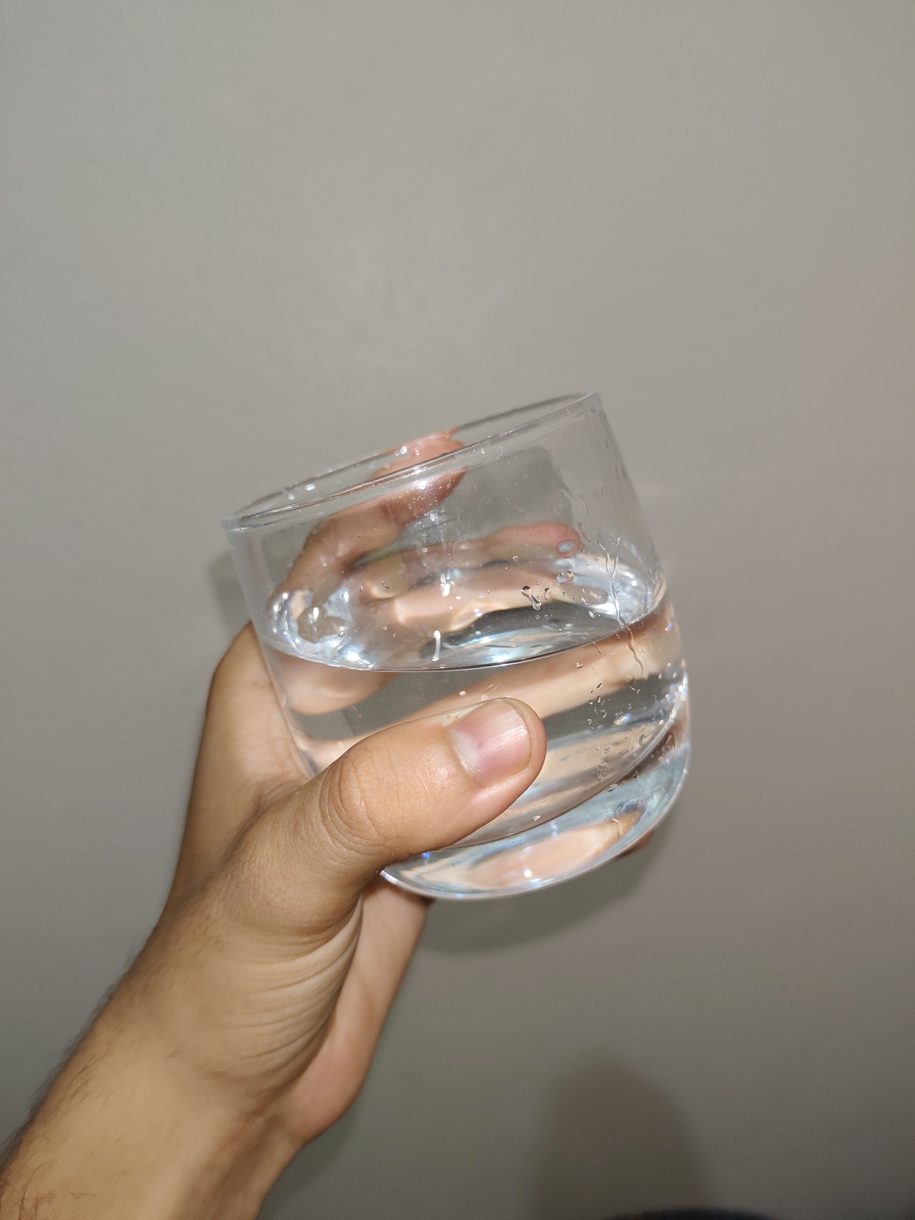 A hand holding a clear glass filled with water, with droplets of condensation on the outside of the glass.