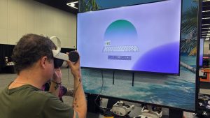A person stands in front of a computer screen, pressing a virtual reality system against their face.
