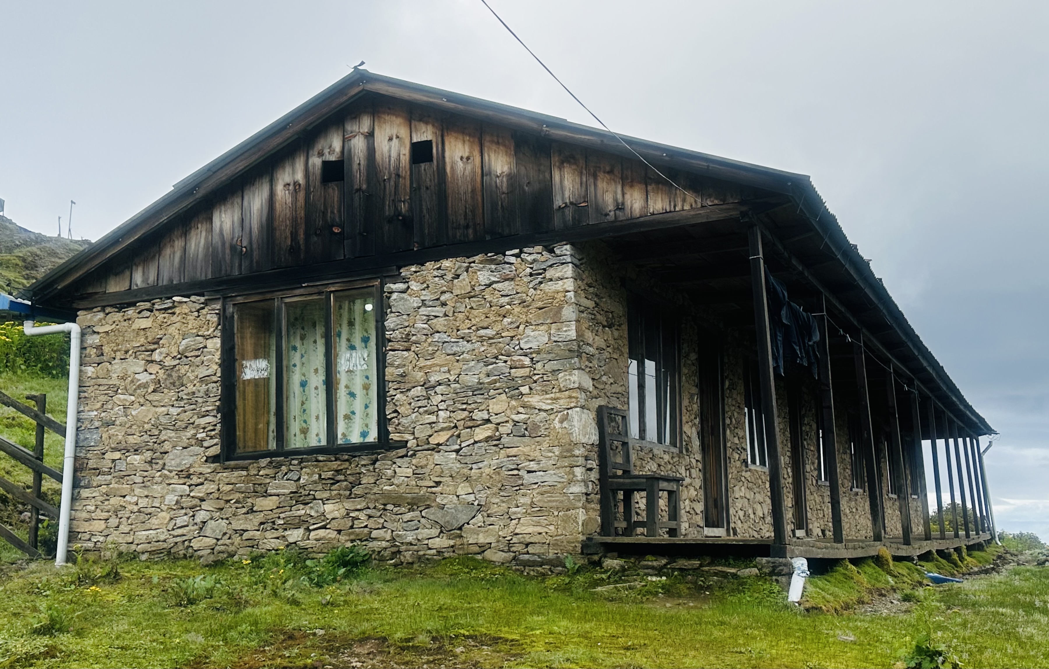 A rustic stone house with a wooden roof and a long porch.