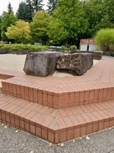 A set of tiled red brick steps leads to a sandy area with large natural stone seats, surrounded by greenery at Washington Park in Portland, captured in the evening with soft natural light. 