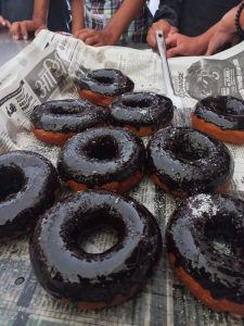 A close-up view of several chocolate-glazed donuts arranged on a surface covered with newspaper. 