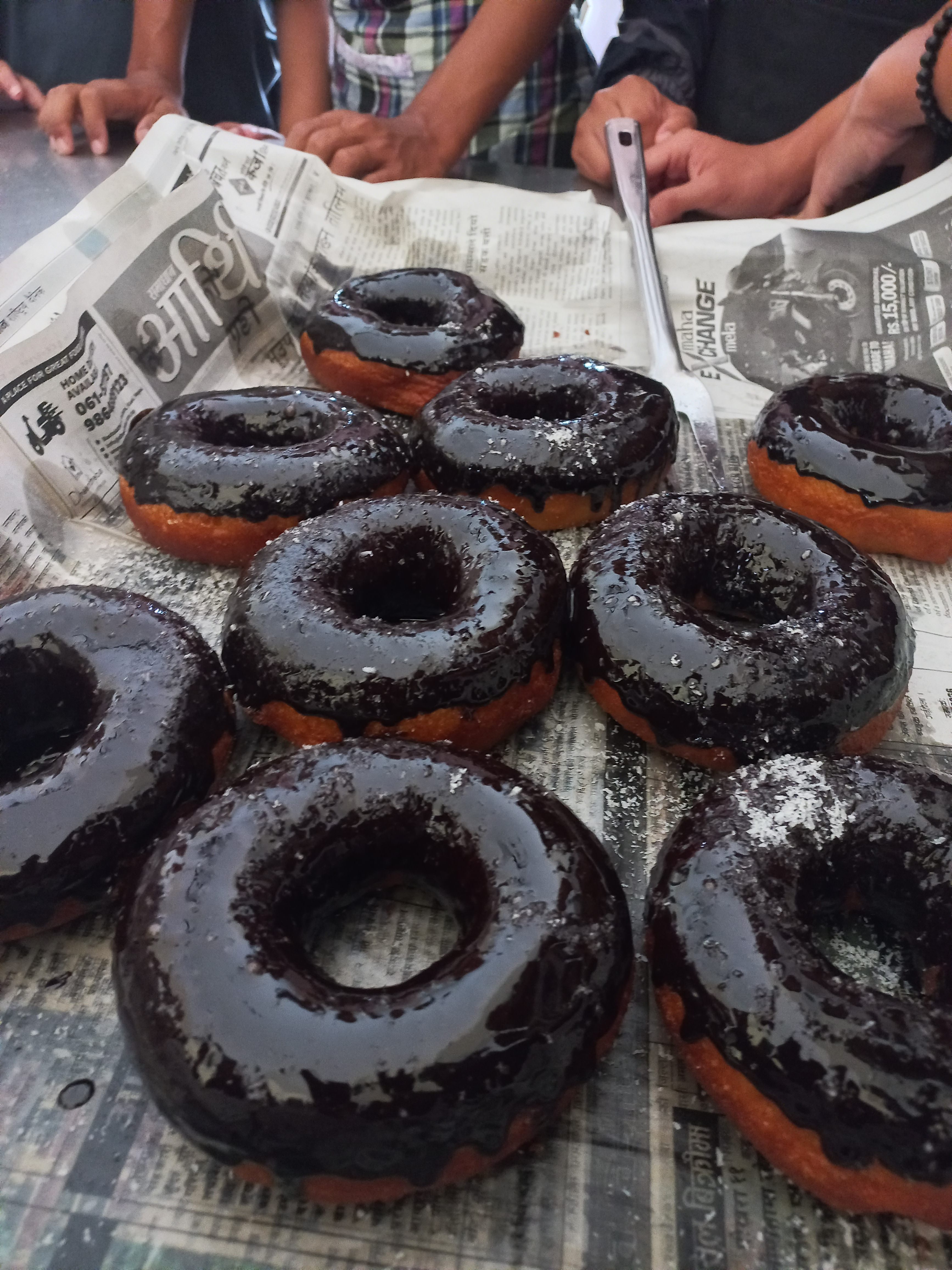 A close-up view of several chocolate-glazed donuts arranged on a surface covered with newspaper. 
