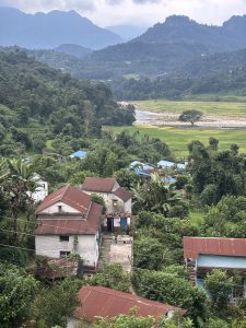 A scenic view of a rural landscape featuring several houses with brown roofs nestled among lush greenery. 