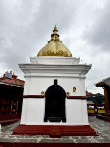 A white and gold pagoda with ornate detailing, set against a cloudy sky. The structure is elevated on a red base, exuding a serene and historical ambiance.