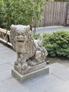 A stone statue of a traditional Japanese lion (shishi) standing guard near bamboo and shrubs. Captured in Portland Japanese Garden.
