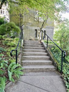 Stone steps leading to the side of the Pittock Mansion, Portland, surrounded by ferns and trees. The photo was taken in the evening, using soft, natural light. 