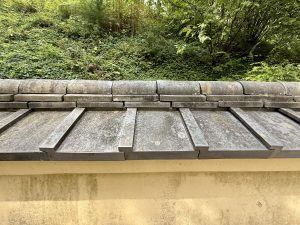 Close-up of a traditional Japanese-style wall with layered roof tiles in the Portland Japanese Garden. Moss and plants grow naturally behind the wall. 