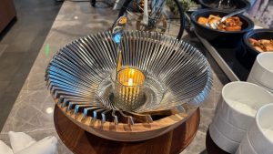 A wooden bowl is shown filled with spoons artfully placed so as to line the wall of the bowl.  In the center is a candle with one spoon sticking up to indicate this is a spoon bowl.