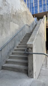 Concrete stairs with a concrete rail go up.  At the top you can see glass windows of an office.