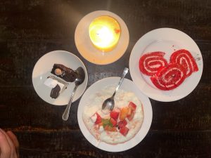 A wooden table is set with three plates of dessert and a lit candle.
