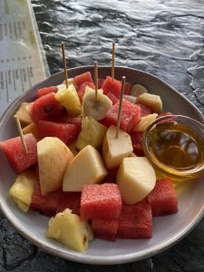 A round plate filled with a colorful assortment of diced fruits, including red watermelon, yellow pineapple, and pale apple, with a slice of banana on top. 
