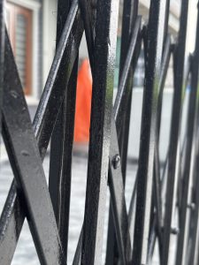 A close-up view of a black metal fence with a crisscross pattern, showcasing shiny, reflective surfaces.