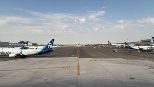 An airport ramp with planes pulled up to gates on the left and right, but only their tails are visible.