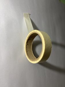A roll of beige masking tape partially unwound, positioned against a light gray background. 