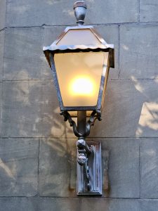 An old-fashioned metal lantern glows warmly on a stone wall. Taken in the evening at Pittock Mansion, Portland. 