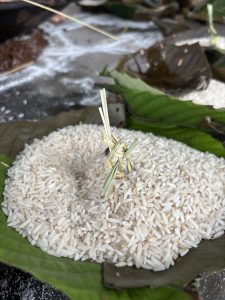 
A pile of uncooked white rice on a green leaf with a small straw decoration in the center.