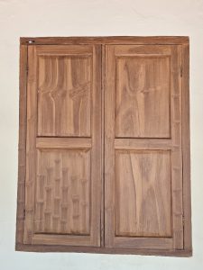 A traditional wooden window with two closed shutters mounted on a white wall, photographed in Kozhikode, Kerala.