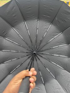 A hand holding a black umbrella from underneath, showing the interior structure with ribs and fabric.
