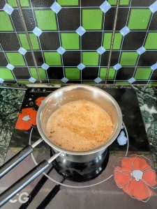 A pot of chai tea is simmering on a black and white stovetop with a green tiled wall in the background.
