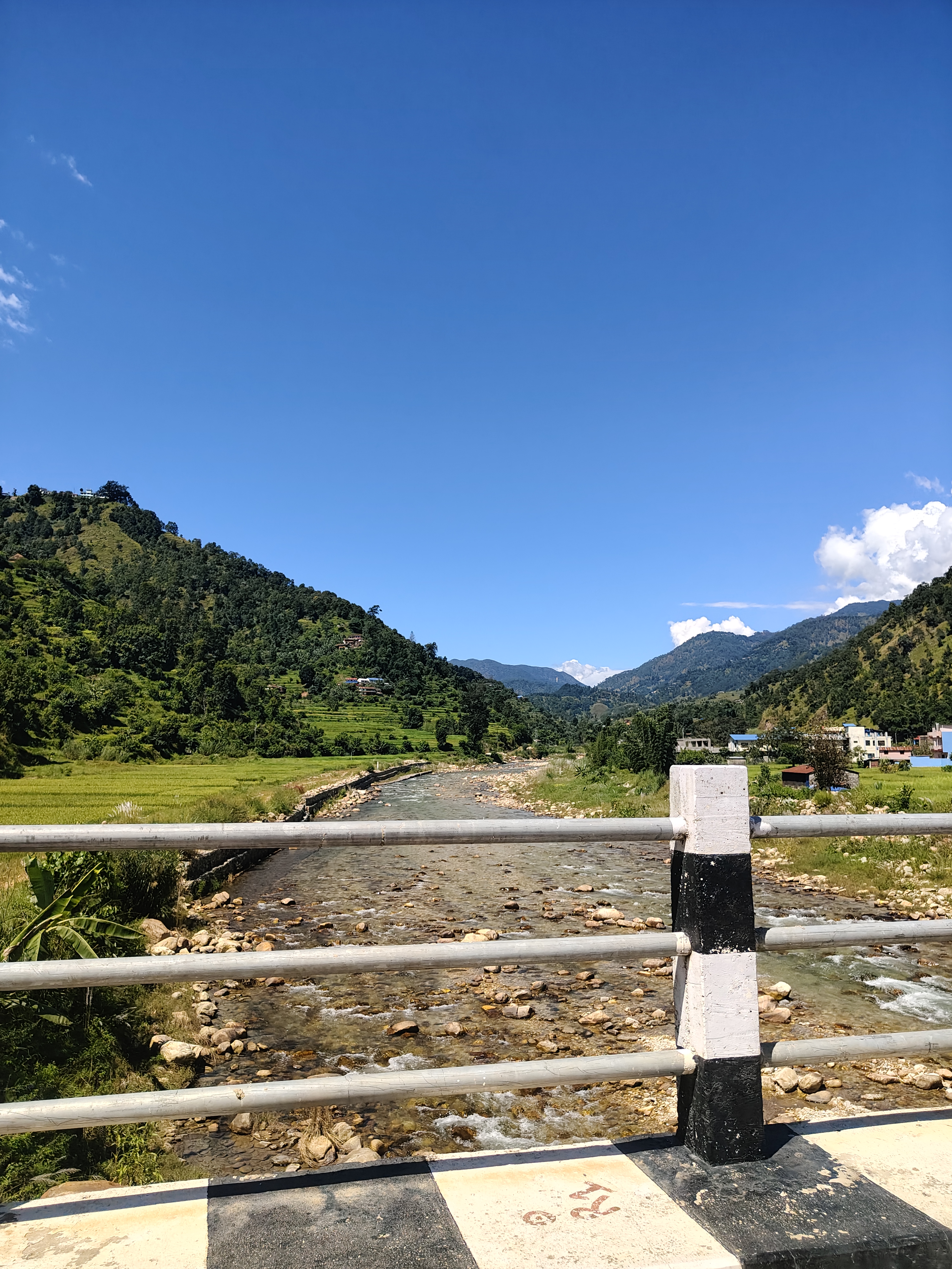 A scenic view from a bridge overlooking a clear river flowing through a valley.