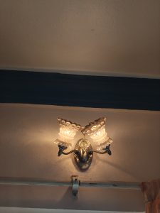 A decorative wall lamp features two glass shades glowing warmly, mounted on a chrome fixture against a neutral-colored wall. 